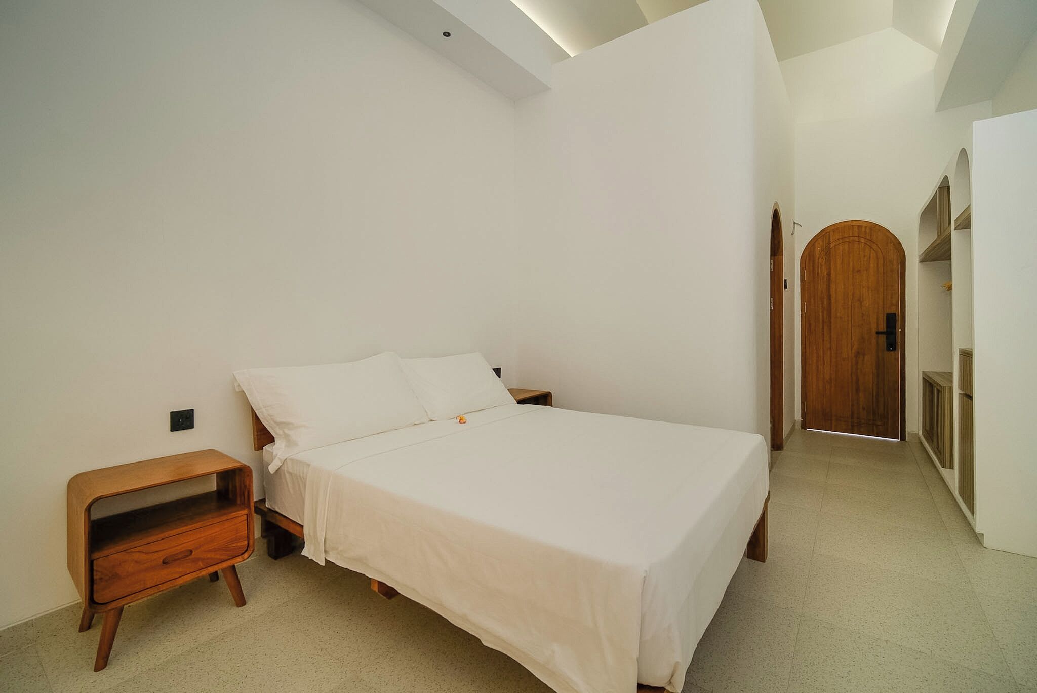 Un dormitorio con cama, una mesita de noche de madera, un armario y una puerta.