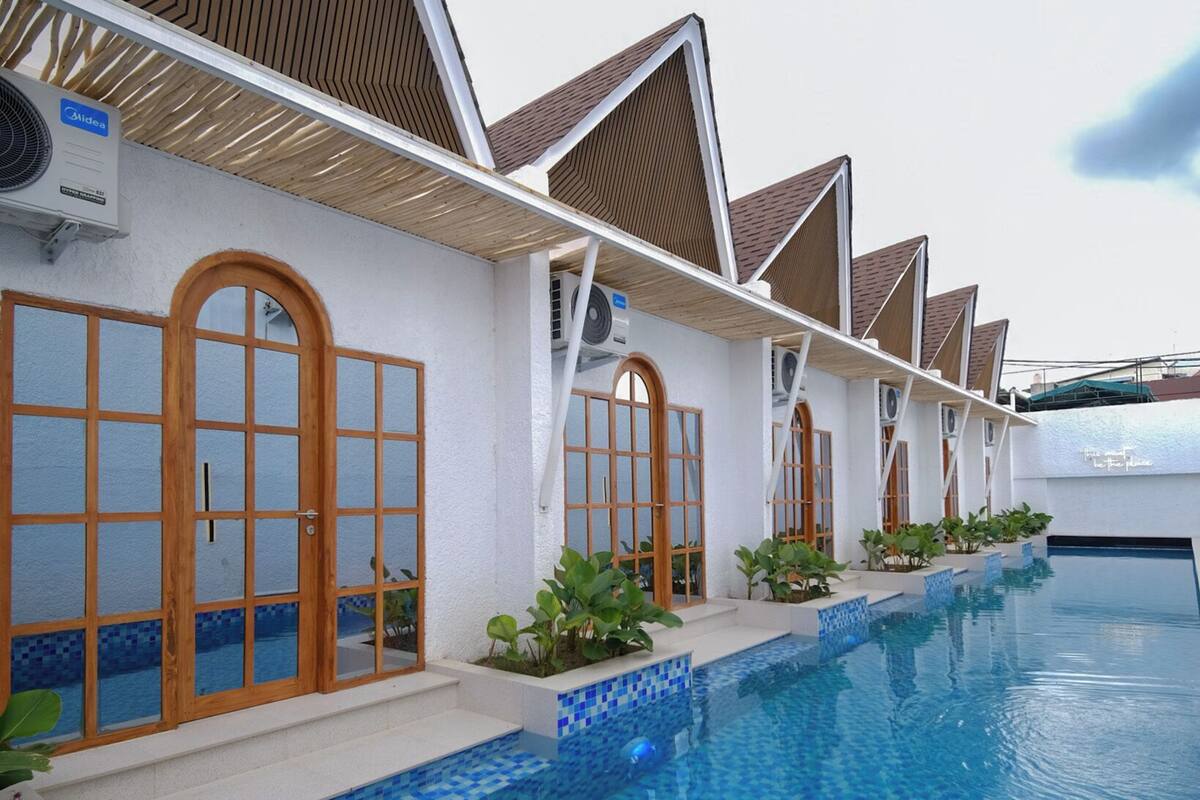 A row of resort-style villas with individual pools, each with a wooden door and a small garden area.