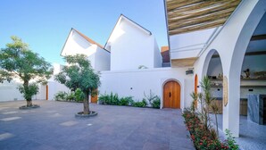 Un patio con un árbol en el centro, paredes blancas y una puerta de madera.