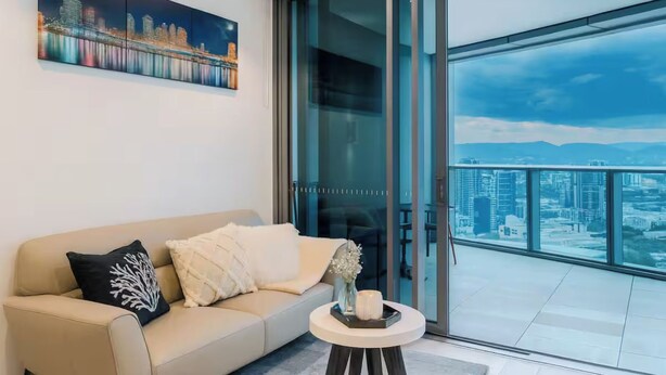 A modern living room with a sofa, a glass door leading to a balcony with a city view. - Gleaming Riverfront - Stay on Casino, Free Carpark (Brisbane City)