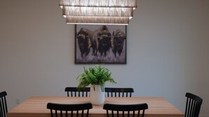 Zona pranzo con tavolo in legno, sedie nere, lampadario e un quadro incorniciato, oltre a una pianta in vaso.