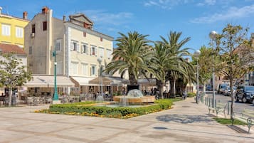 Una plaza pública con una fuente, palmeras y mesas al aire libre en un café.