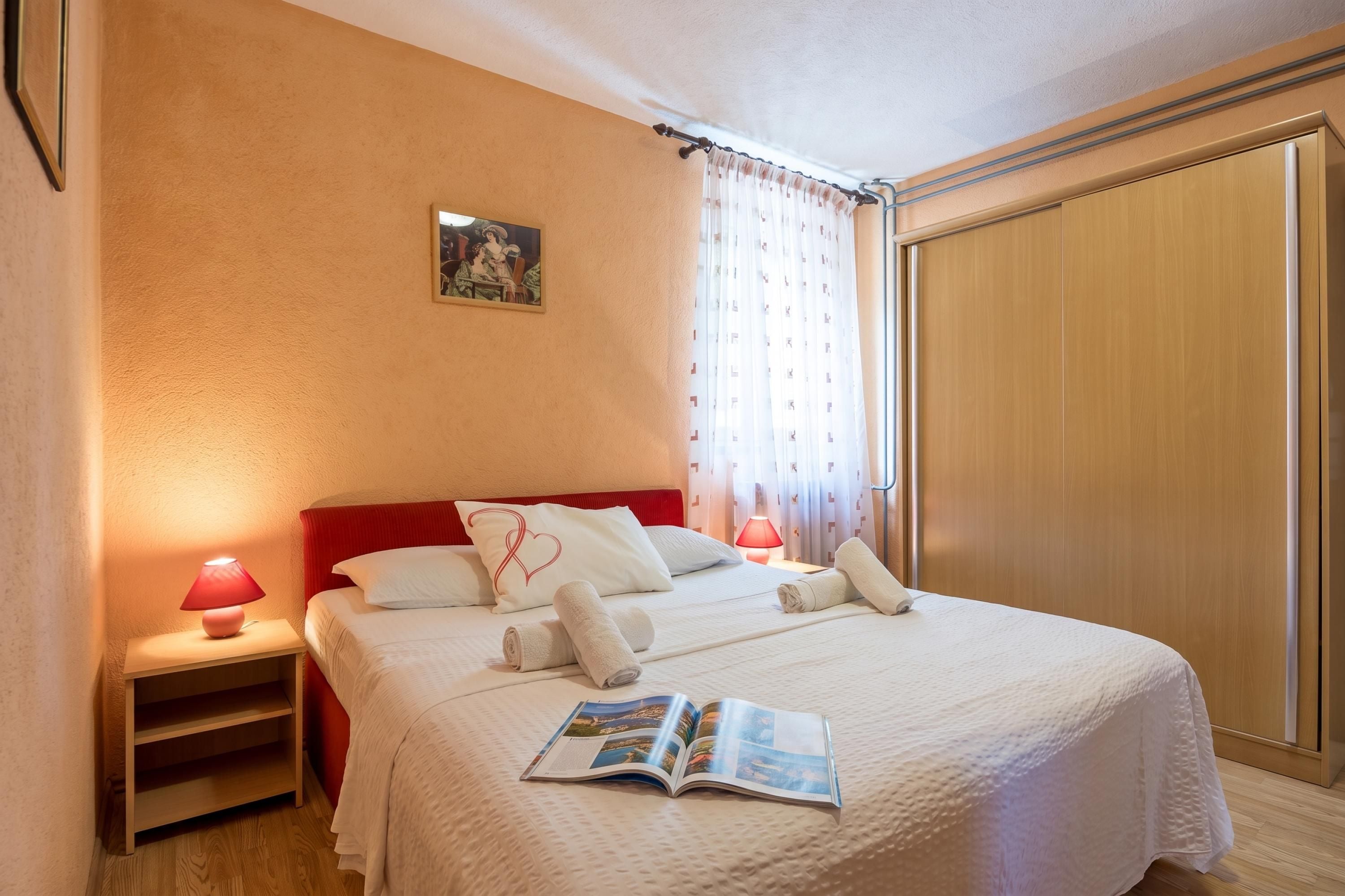 A hotel room with a bed, a nightstand, a reading lamp, a window with curtains, and a wardrobe.