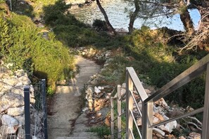 A stone pathway leading to a body of water, surrounded by greenery and a metal railing. - Amalija sea View Apartments (Mali Losinj)