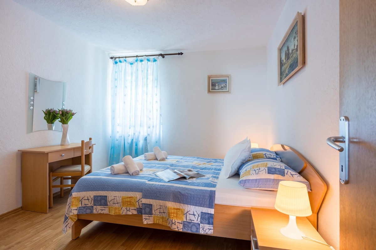 Quarto com cama, mesa de cabeceira, luminária e escrivaninha com cadeira.