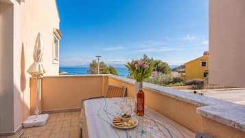 A balcony with a table set for two, a vase with flowers, and a view of the sea.
