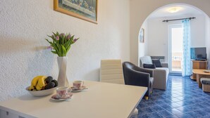 Ett rum med ett matbord, en vas med blommor, en skål med frukt, en soffa och en tv.