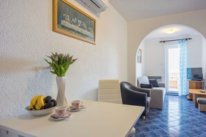 A room with a dining table, a vase with flowers, a bowl of fruit, a sofa, and a television. - Amalija sea View Apartments (Mali Losinj)
