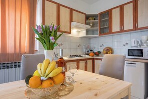 Une cuisine avec des meubles de rangement en bois, une table à manger ornée d’un panier de fruits, une bouteille de vin et un verre.