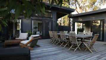 A modern outdoor deck with a wooden table and chairs, surrounded by glass doors and windows.