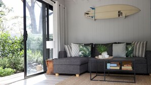 Un soggiorno moderno con un divano angolare grigio, un tavolino da caffè e una tavola da surf appesa al muro.