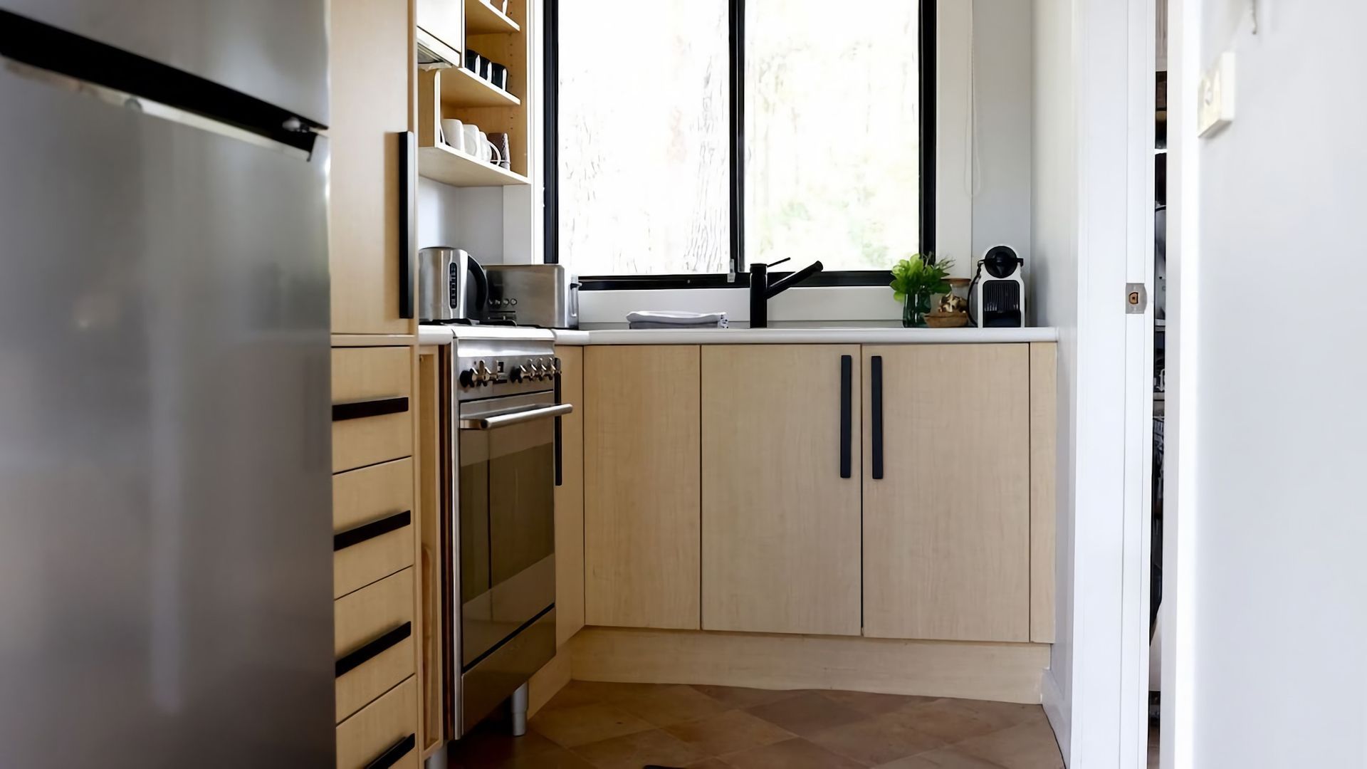 A compact kitchen with a built-in oven, a coffee maker, and a window above the sink.