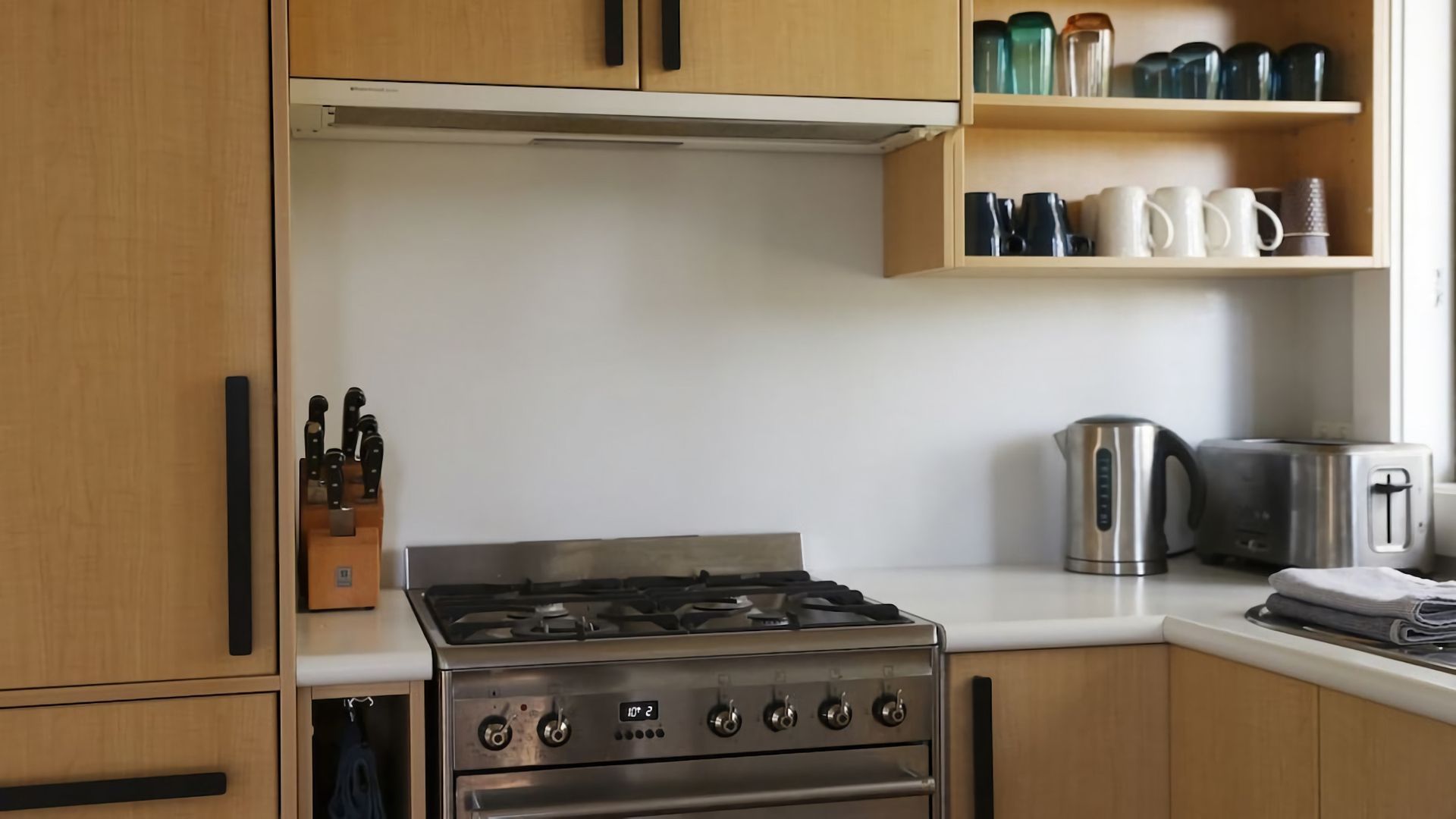 A kitchen with wooden cabinets, a stainless steel stove, a kettle, and a toaster.