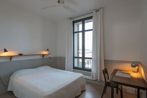 A hotel room with a bed, a desk, a chair, a window with curtains, and a ceiling fan. - magnificent 2 bedrooms with sea and salt marsh views (Porto-Vecchio)