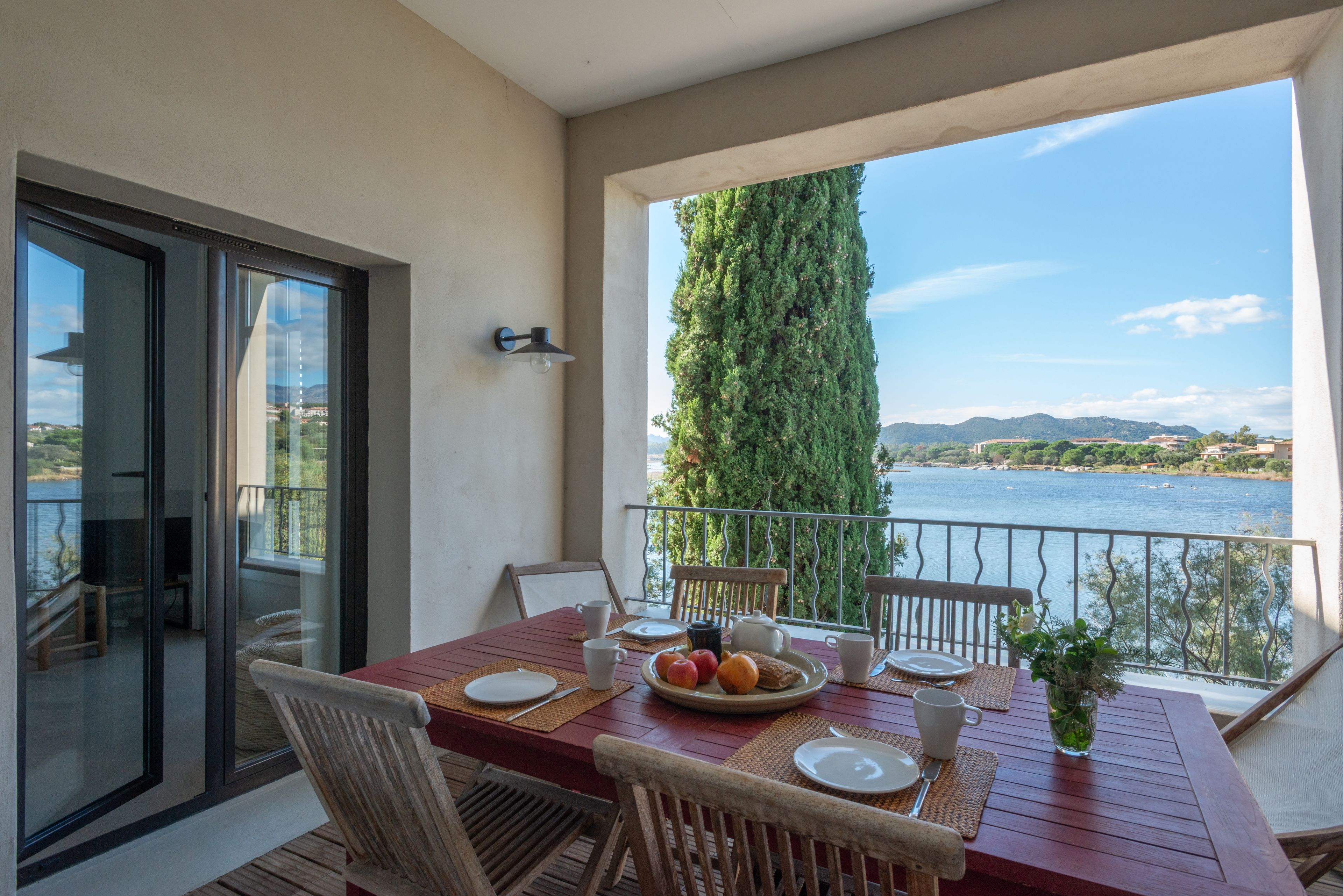 A balcony with a table set for dining, overlooking a body of water and a mountainous landscape.