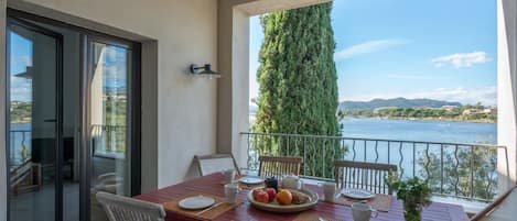 A balcony with a table set for dining, overlooking a body of water and a mountainous landscape.