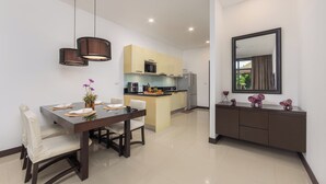 Une cuisine moderne dotée d’un îlot central, d’un coin repas avec une table en bois foncé et des chaises blanches, et d’un grand miroir au mur.