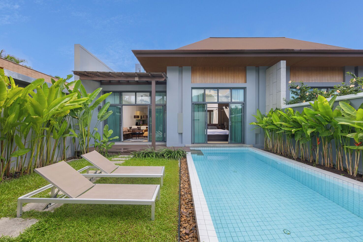 A modern house with a swimming pool, a dining area, and a bedroom visible through the glass doors.