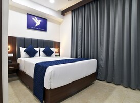 Habitación de hotel con una cama grande, cabecera de madera oscura, ropa de cama blanca y una manta acolchada azul. Hay una lámpara de pared y una cita inspiradora enmarcada sobre la cama.