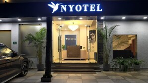 A hotel entrance with a reception desk, a staircase, and potted plants. - Nyotel (Bhopal)