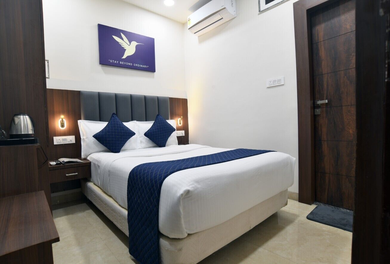 A neatly arranged hotel room with a bed, bedside tables, a coffee maker, and a wall-mounted air conditioner.