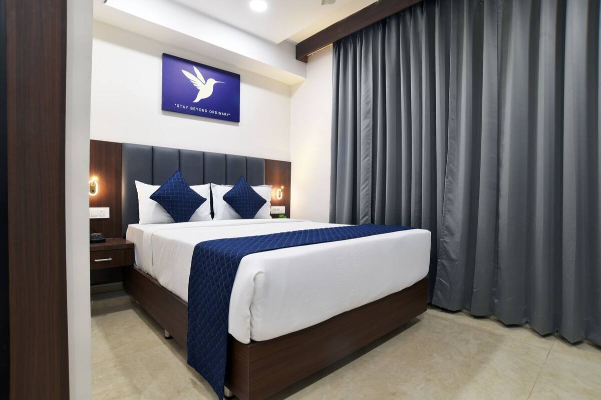 A modern hotel room with a large bed, dark wood headboard, white bedding, and a blue quilted throw.