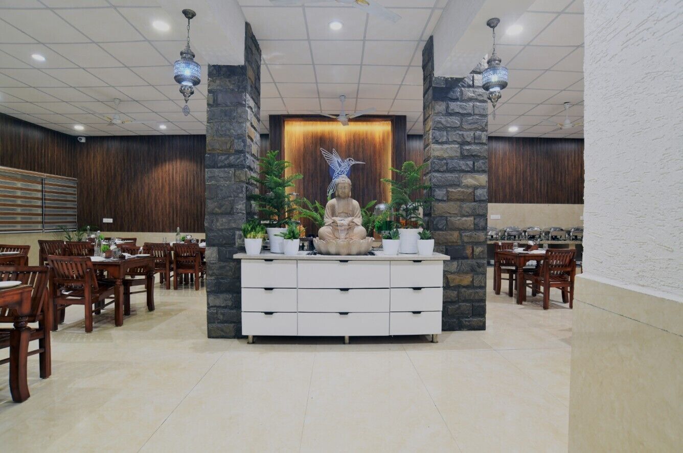 Ein Essbereich mit Holztischen und -stühlen, ein zentral platziertes weißes Buffet mit Blumentöpfen und eine dekorative Statue.