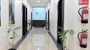 A hallway with potted plants, a fire extinguisher, and a door with a bird logo. - Nyotel (Bhopal)