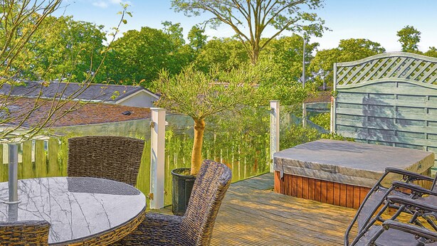 Une terrasse dotée de meubles en osier, d’un jacuzzi et d’une clôture en bois.