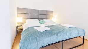 Una cama bien hecha con colcha azul, dos lámparas de noche y cabecero gris.