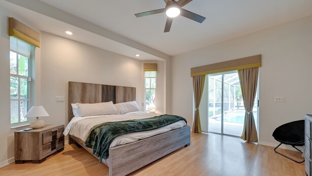 Une chambre moderne avec un lit en bois, une table de chevet, un ventilateur de plafond et une vue sur une piscine.