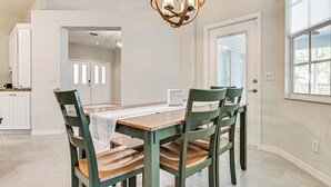Un coin repas avec une table et des chaises en bois, un lustre et une vue sur la cuisine.