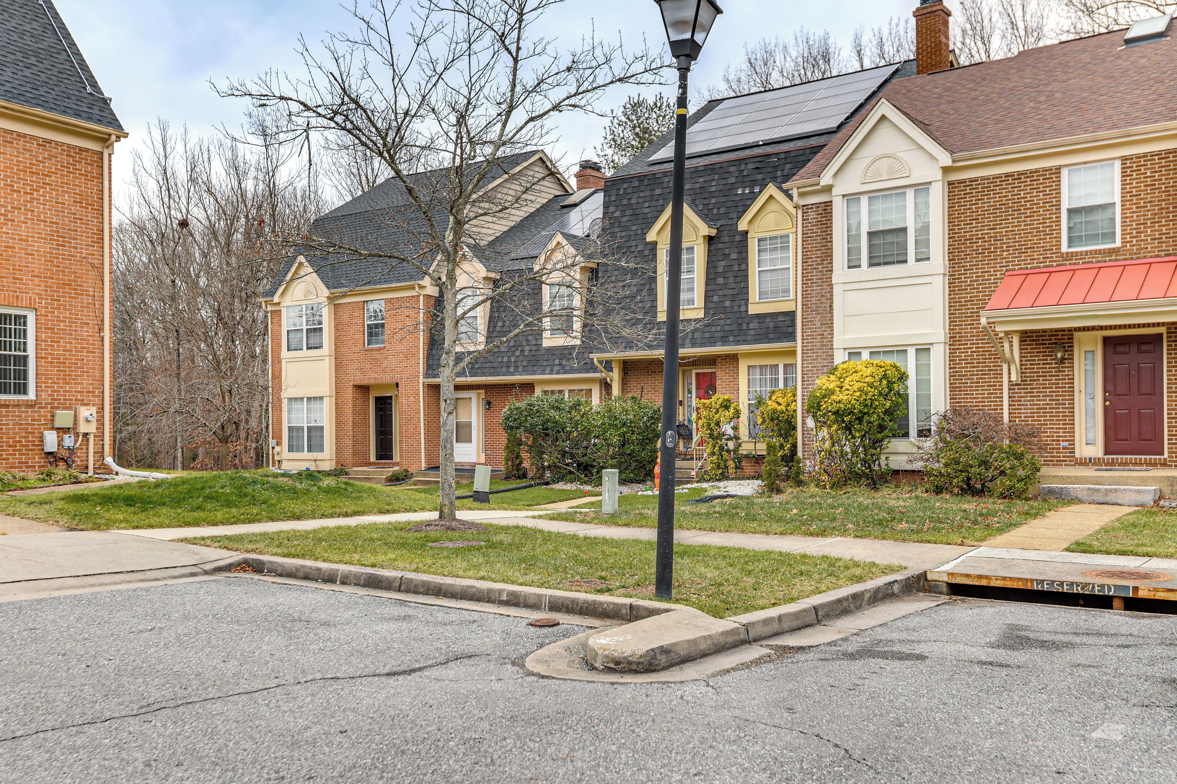 A row of townhouses with brick exteriors, a small front yard, and a street lamp.