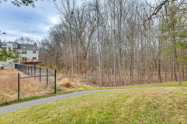 A fenced park area with a paved path, surrounded by leafless trees and a residential building.