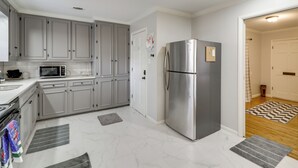Una cocina moderna con armarios grises, un refrigerador de acero inoxidable, un microondas y piso de baldosas.