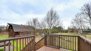 Une terrasse en bois avec une rambarde, une vue sur une maison et une pelouse.