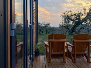 A wooden deck with two wooden chairs, a glass door, and a view of trees and sky.