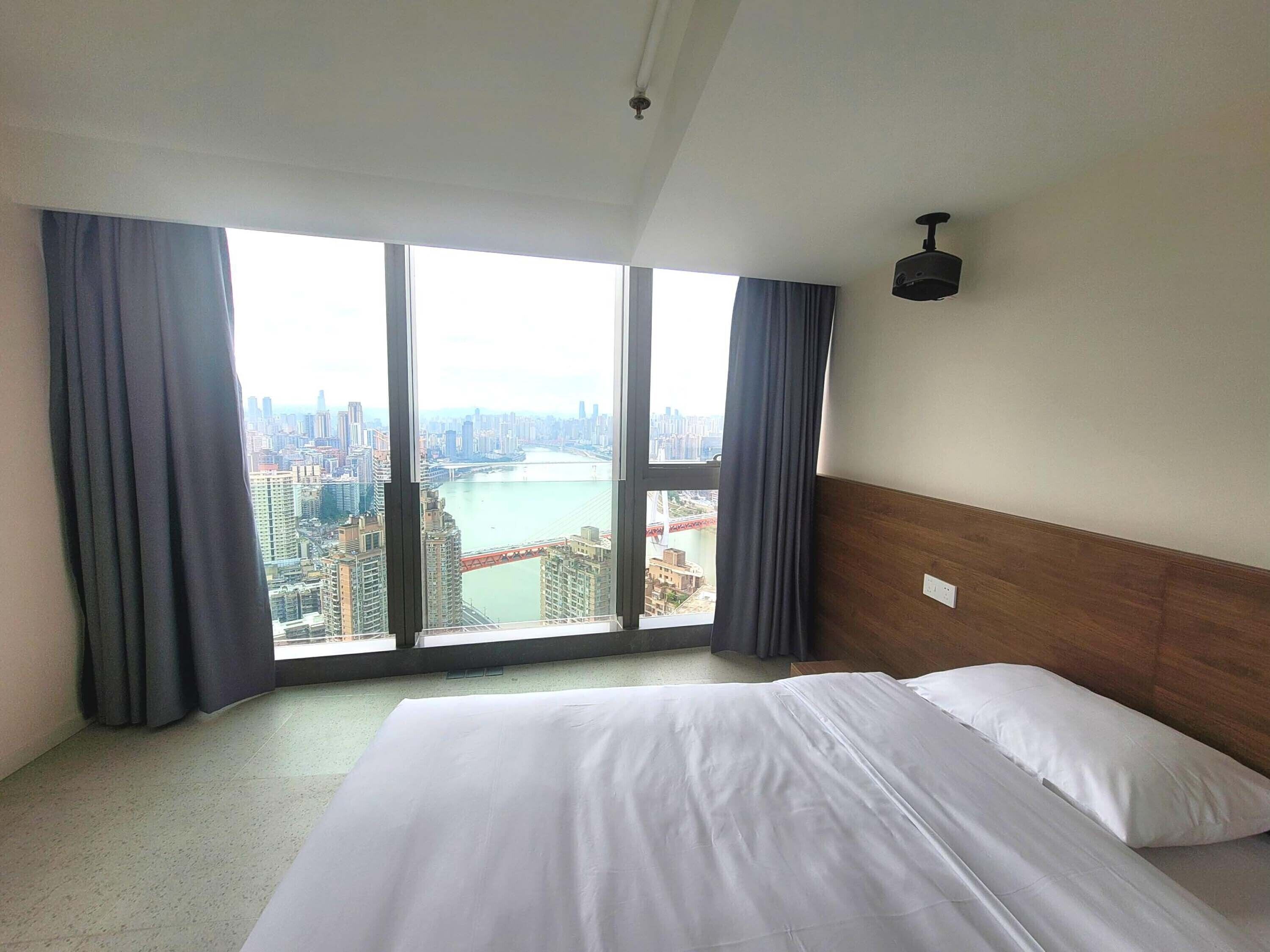 A hotel room with a large bed, a view of a cityscape, and a river.