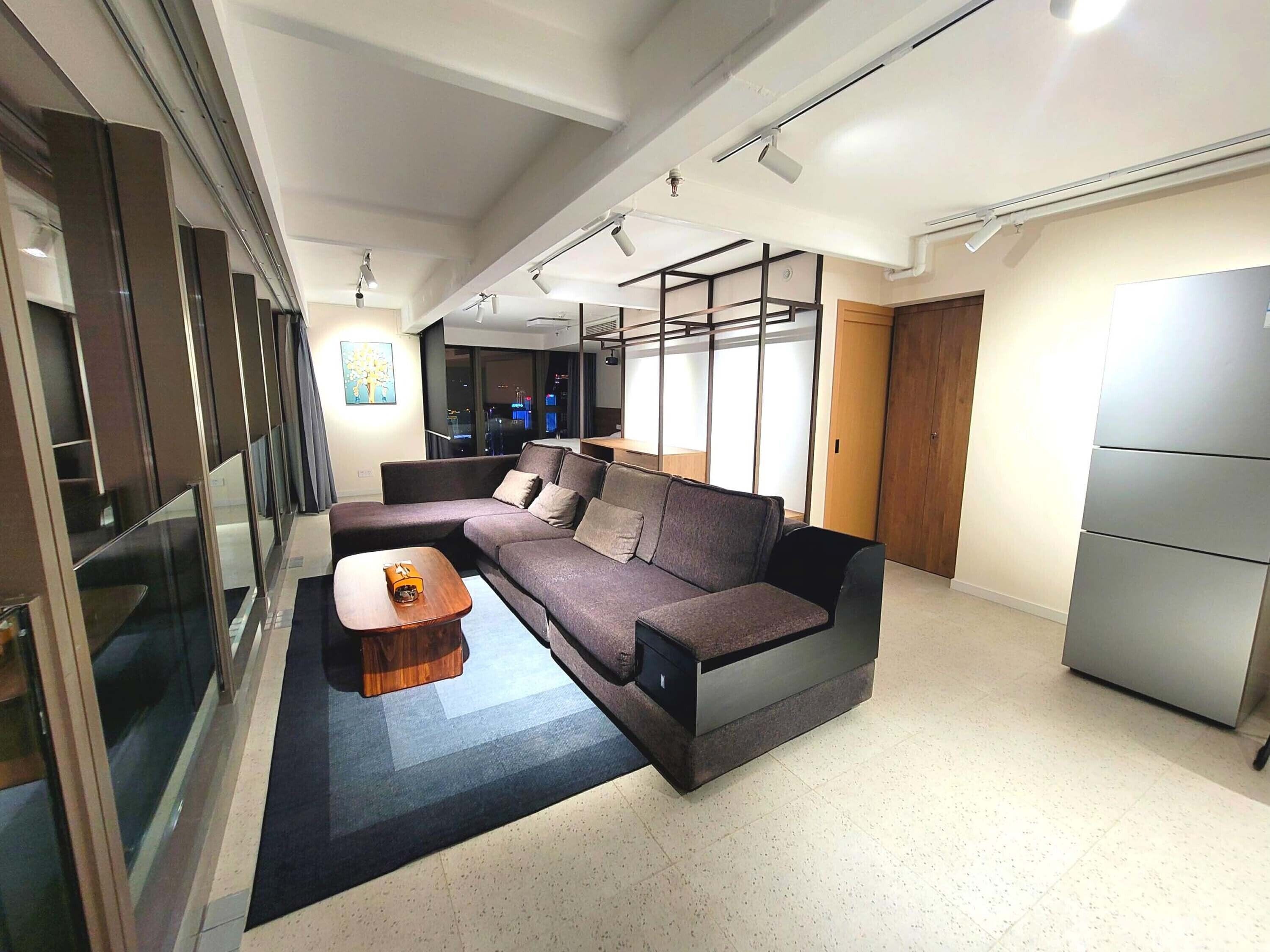 A modern living room with a sectional sofa, a wooden coffee table, and a glass partition.