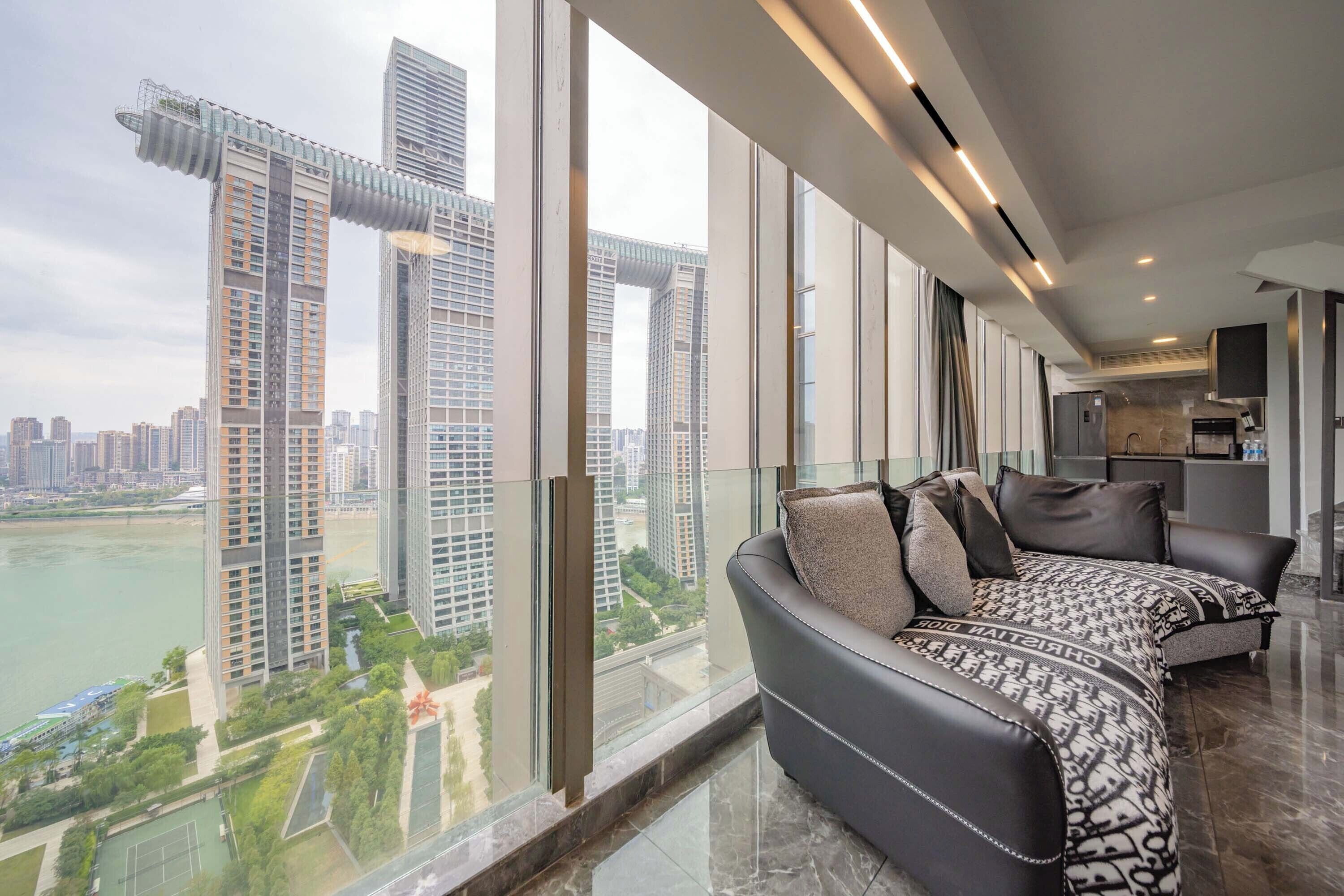 A modern living room with a large window, a sofa, and a kitchen area.