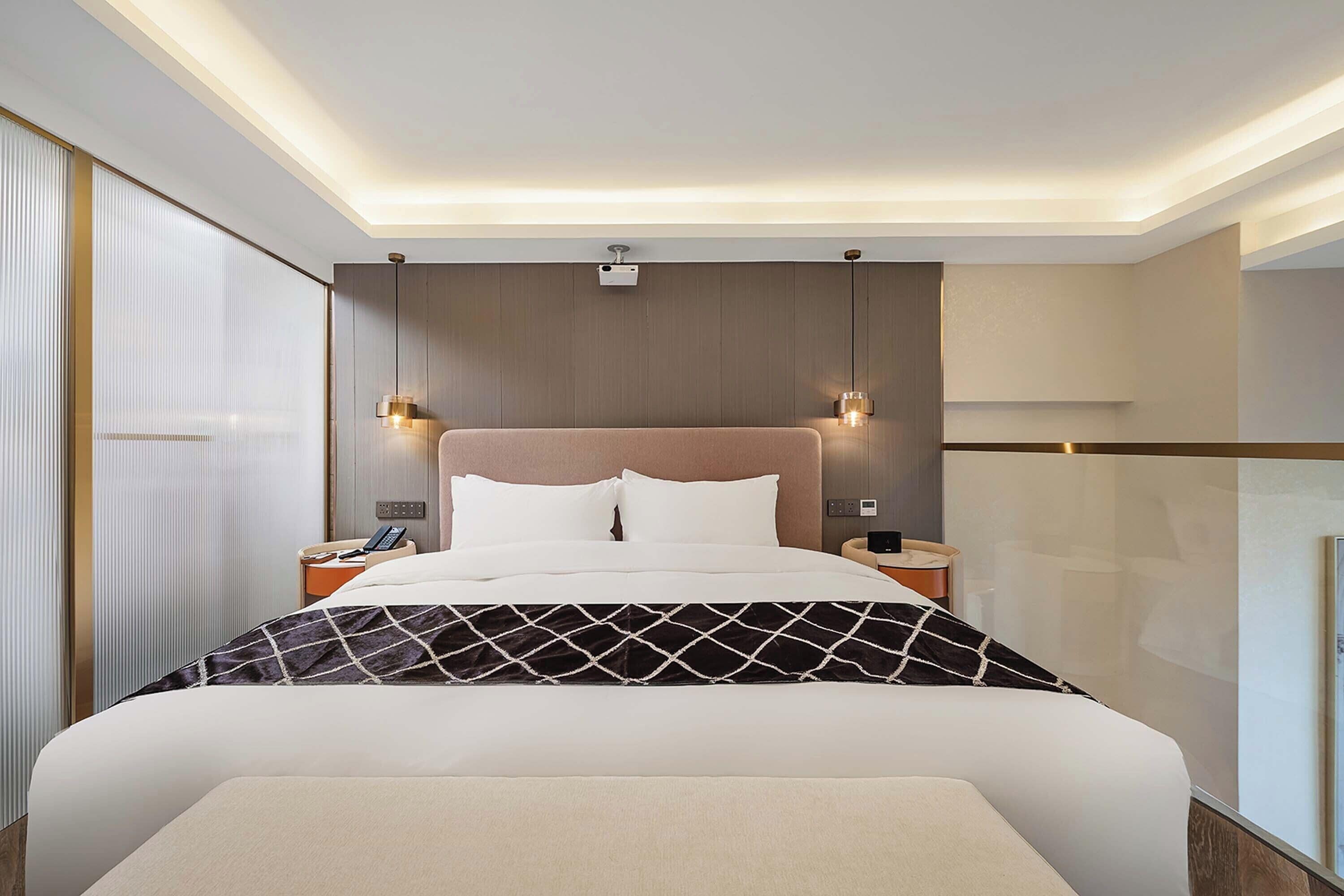 Ein modernes Hotelzimmer mit einem großen Bett, Nachttischen und einer Deckenleuchte.