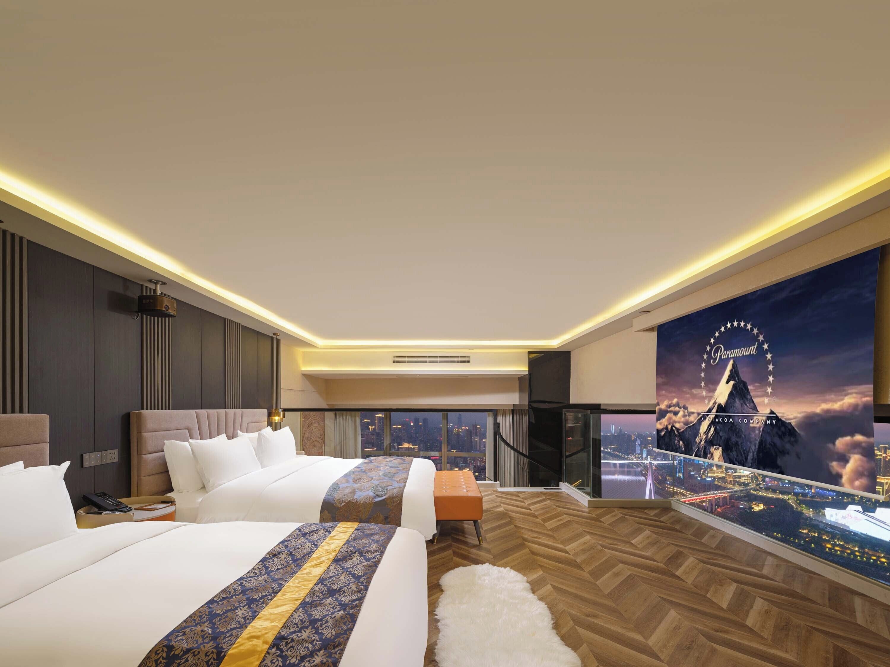 A hotel room with two beds, a large window with a city view, a mounted TV, and a Paramount movie theater poster.