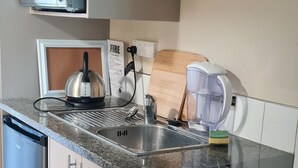 Una cocina equipada con microondas, hervidor, cafetera y tabla de cortar de madera.