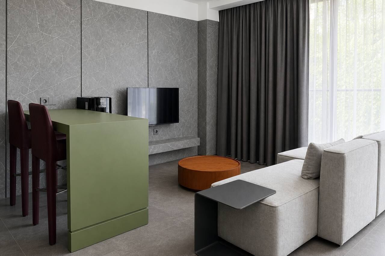 A modern living space with a green kitchen island, a grey sofa, and a flat-screen TV mounted on a grey wall.