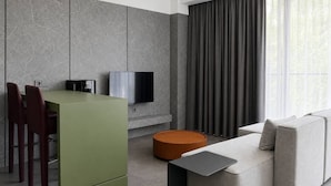 Un espacio habitable moderno con una isla de cocina verde, un sofá gris y un televisor de pantalla plana montado en la pared.