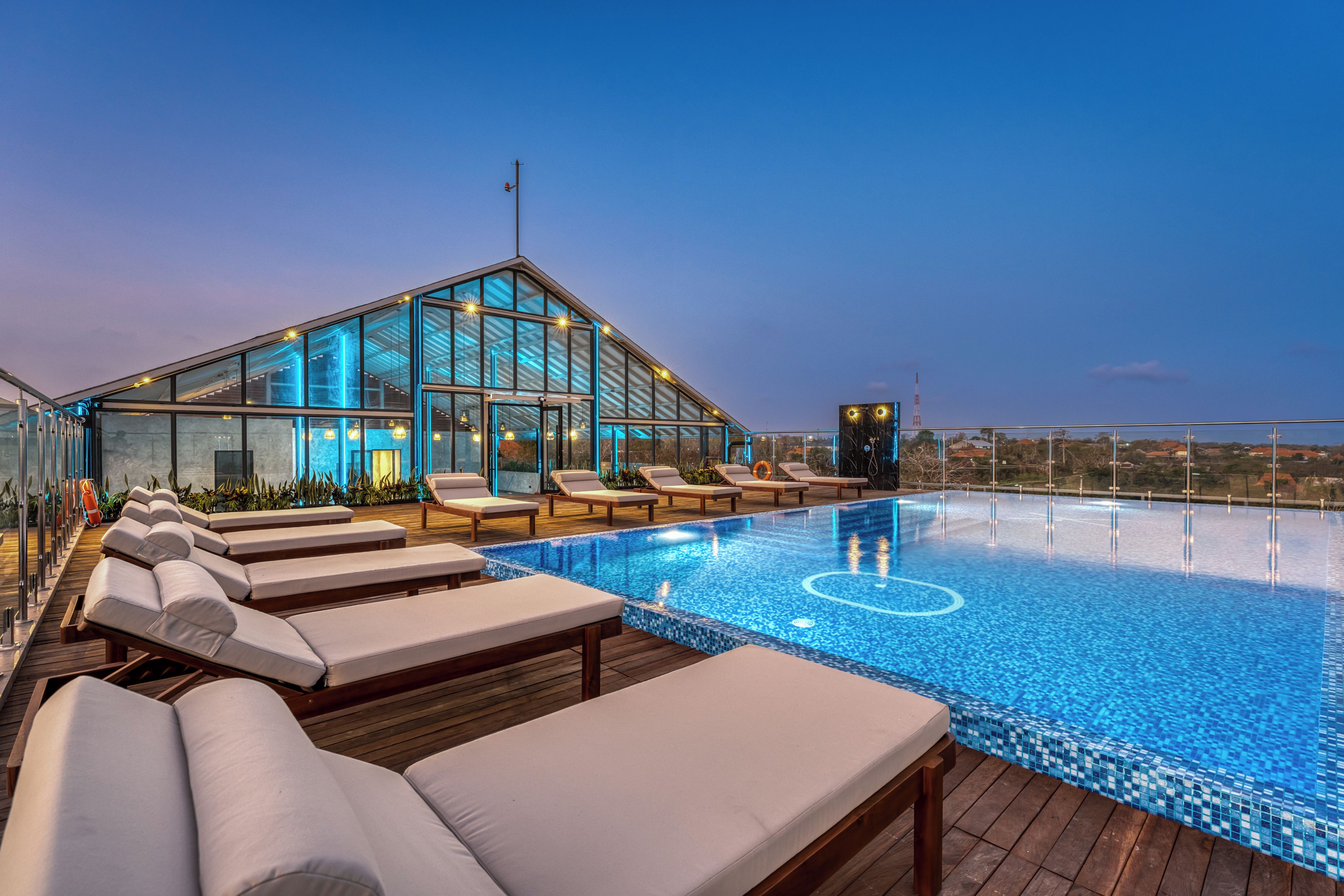 A rooftop infinity pool with lounge chairs and a glass-enclosed structure.