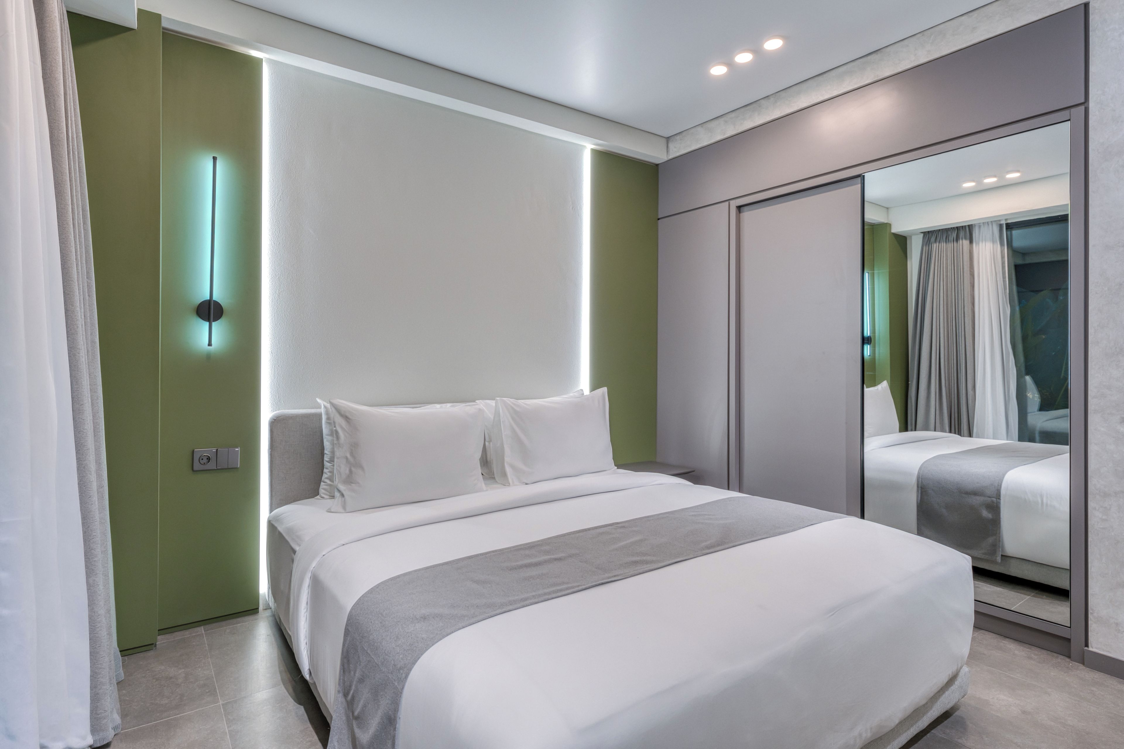 Una habitación de hotel moderna con una cama grande, un espejo y una pared verde de acento.