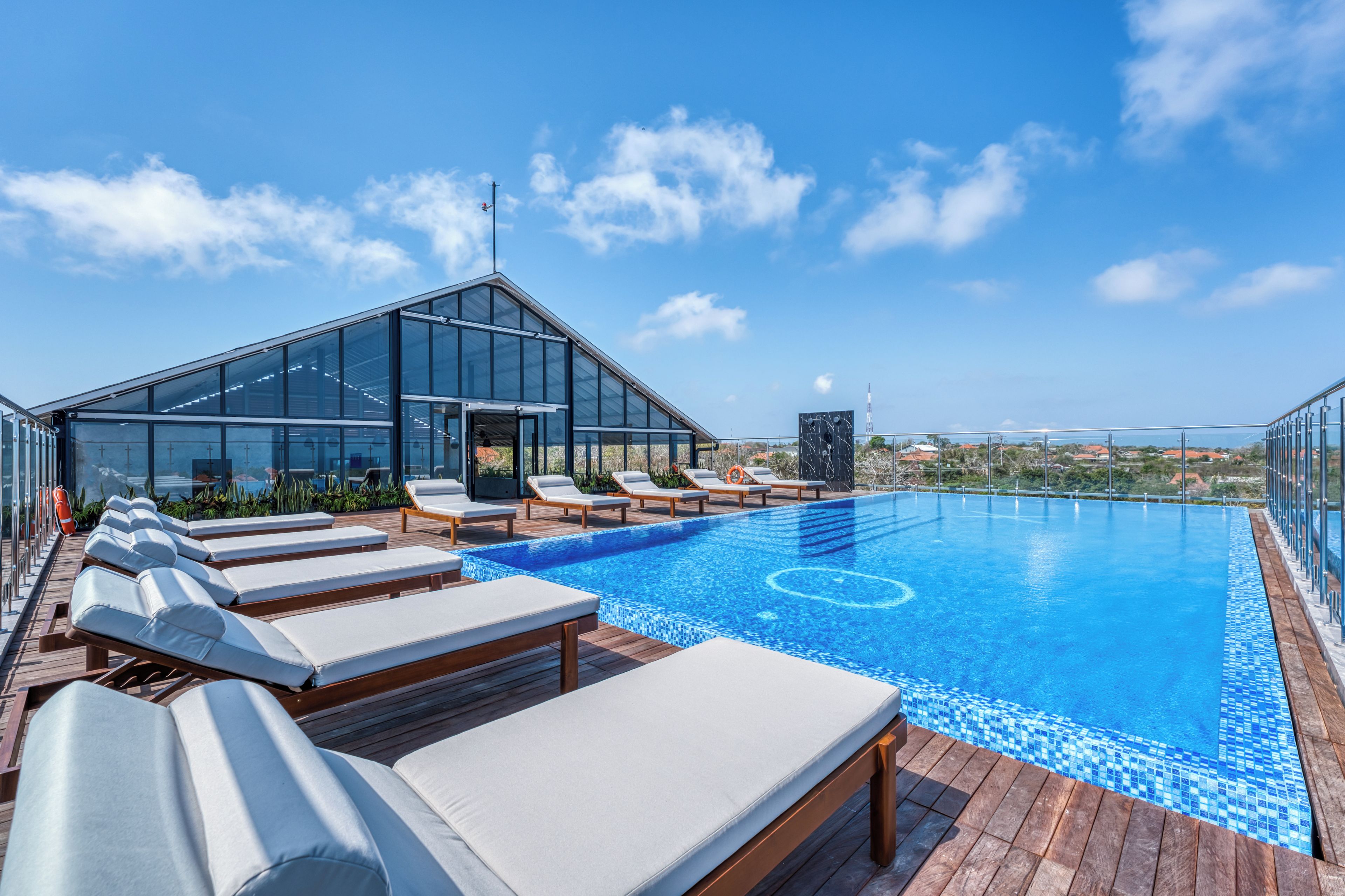 Una piscina en la azotea con sillones de descanso y una estructura de cristal.