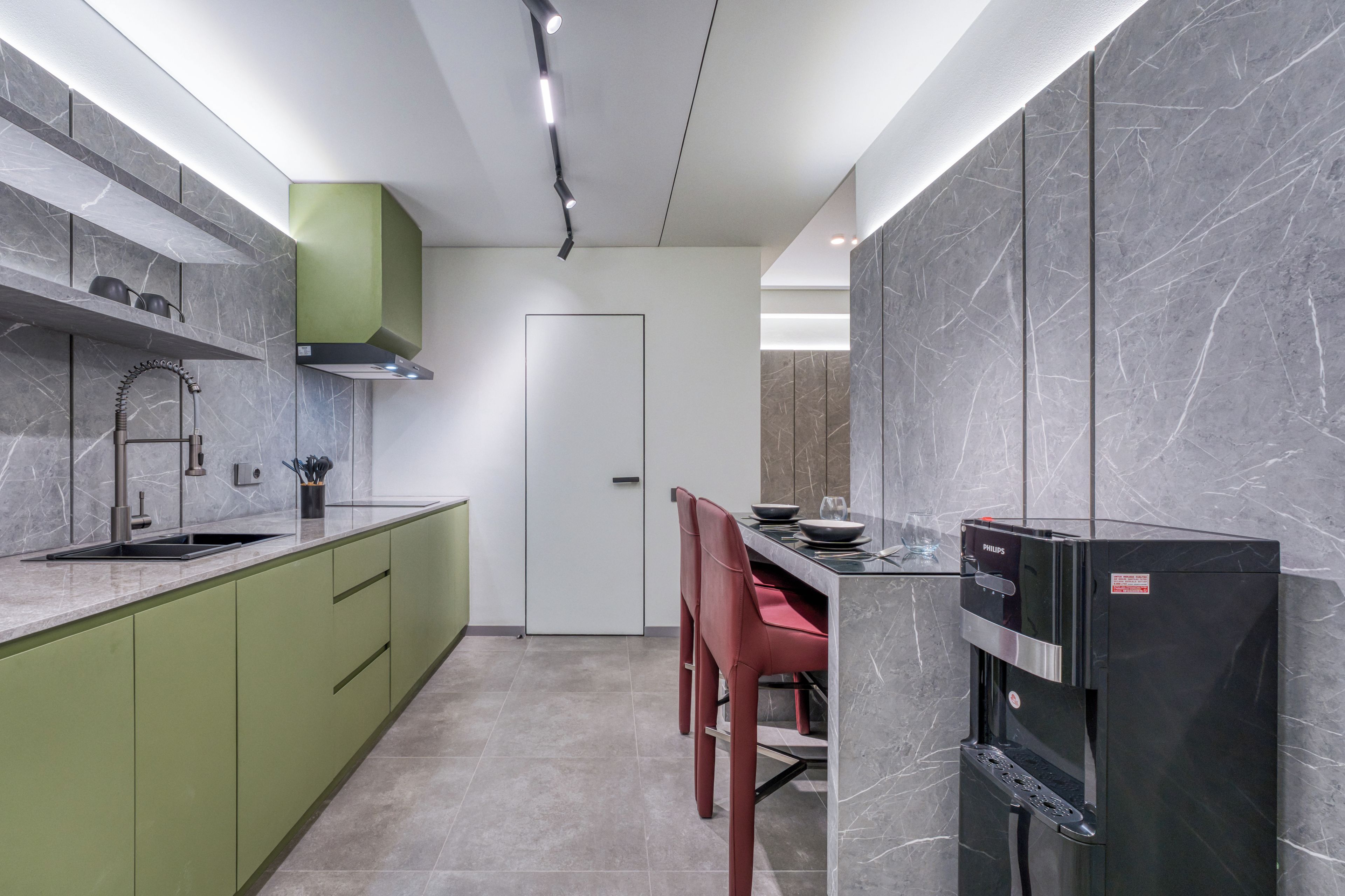 A modern kitchen with a built-in dishwasher, a green cabinet, and a dining area with red chairs.