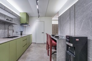 A modern kitchen with a built-in dishwasher, a green cabinet, and a dining area with red chairs. - XO PANDAWA Adult Only (Kutuh)